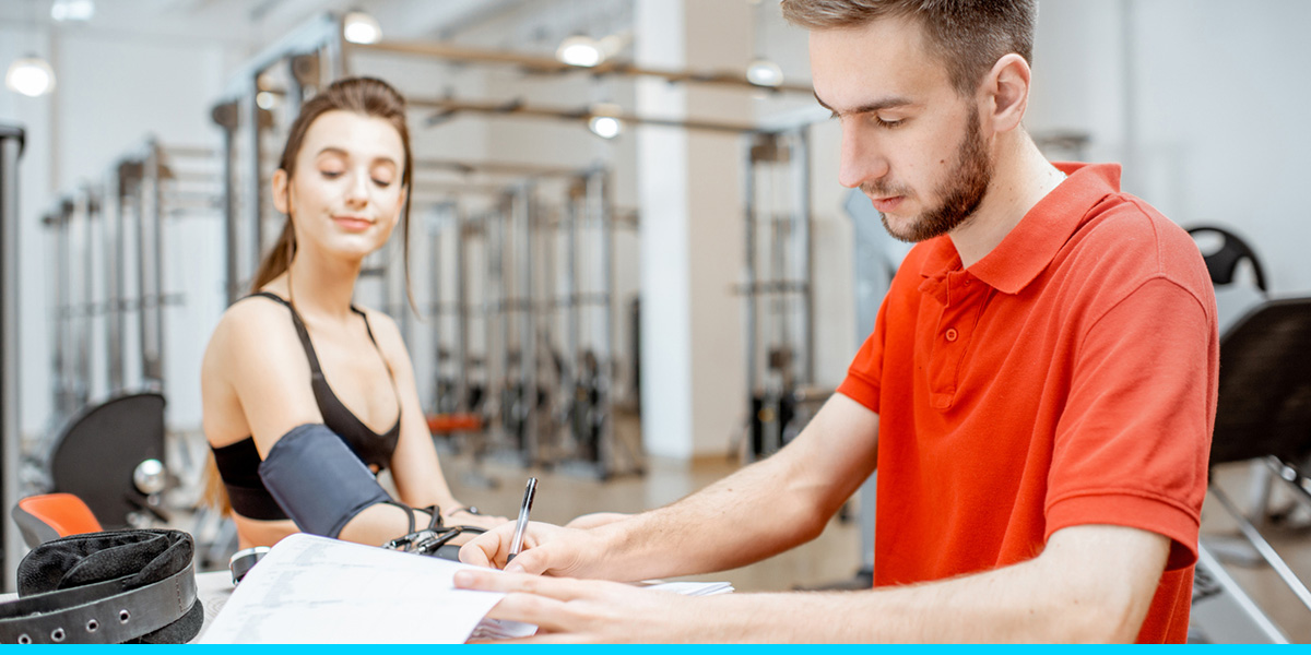 A man in a red shirt is providing nutrition counseling to a girl with a heart rate monitor on her arm